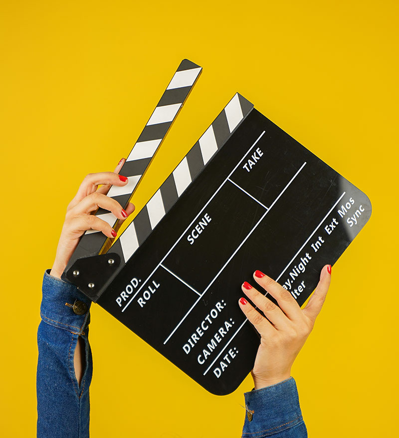 A film production clapper board is held aloft in front of a bright yellow background